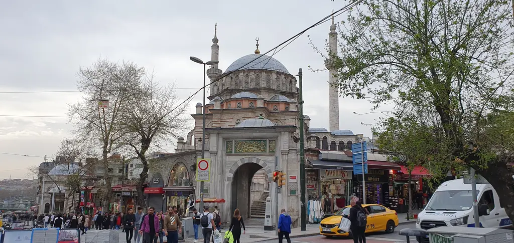 Ordu Caddesi'nden Laleli Camii; caddede yayalar ve araçlar, kaldırım boyunca ağaçlar, arkada külliyenin kapısı ile caminin kütlesi.