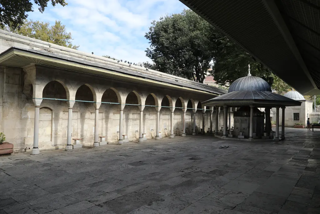 Kılıç Ali Paşa Camii'nin avlusu; mermer sütunlara oturan uzun revak, taş döşeli zemin ve sağda kubbeli şadırvan.
