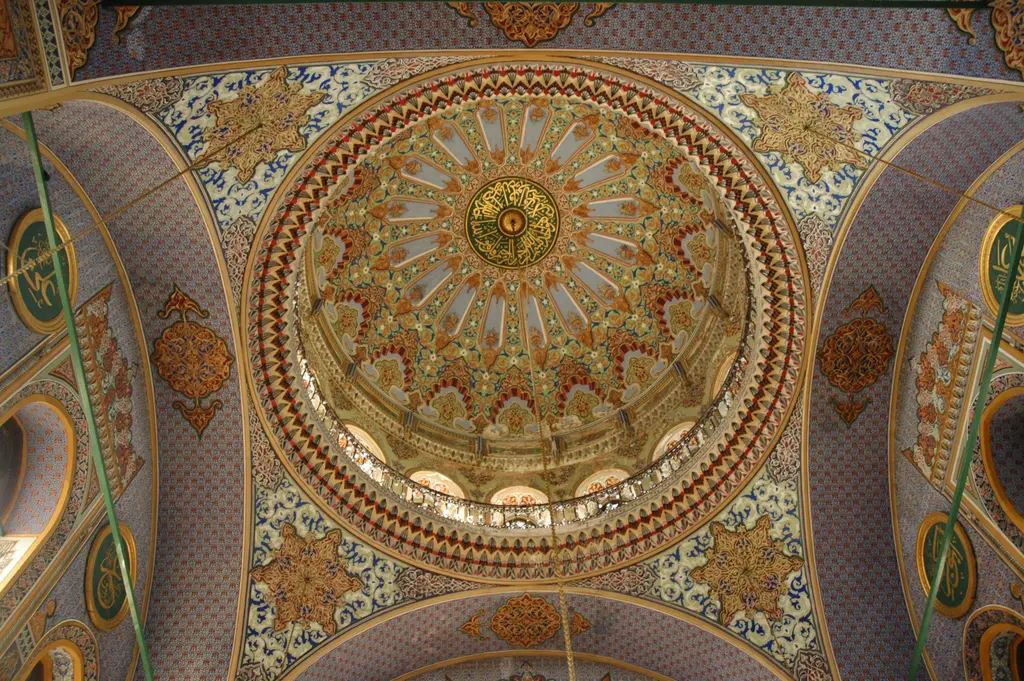 Pertevniyal Valide Sultan Camii'nin kubbesi; altın ve kırmızı bitki motifleri, ortada yazılı göbek, çevrede yarım kubbe yüzeyleri.