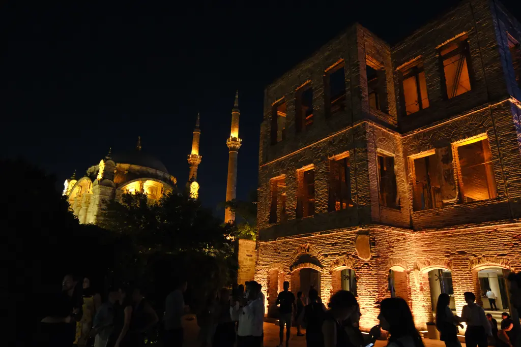 Gece Esma Sultan Yalısı ve yanında Ortaköy Camii; aydınlatılmış kubbe ve minareler, ışıklı tuğla duvarlar.
