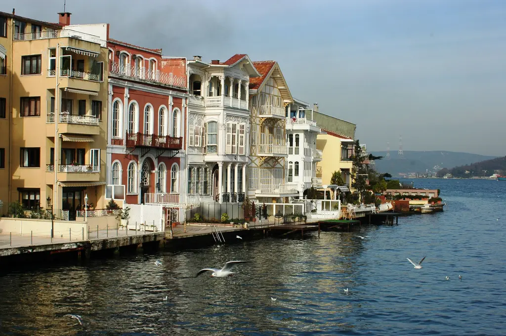 Yeniköy kıyısında yan yana dizilen yalılar; sarı, kırmızı ve beyaz cepheler, ahşap balkonlar ve önde martıların uçtuğu Boğaz.