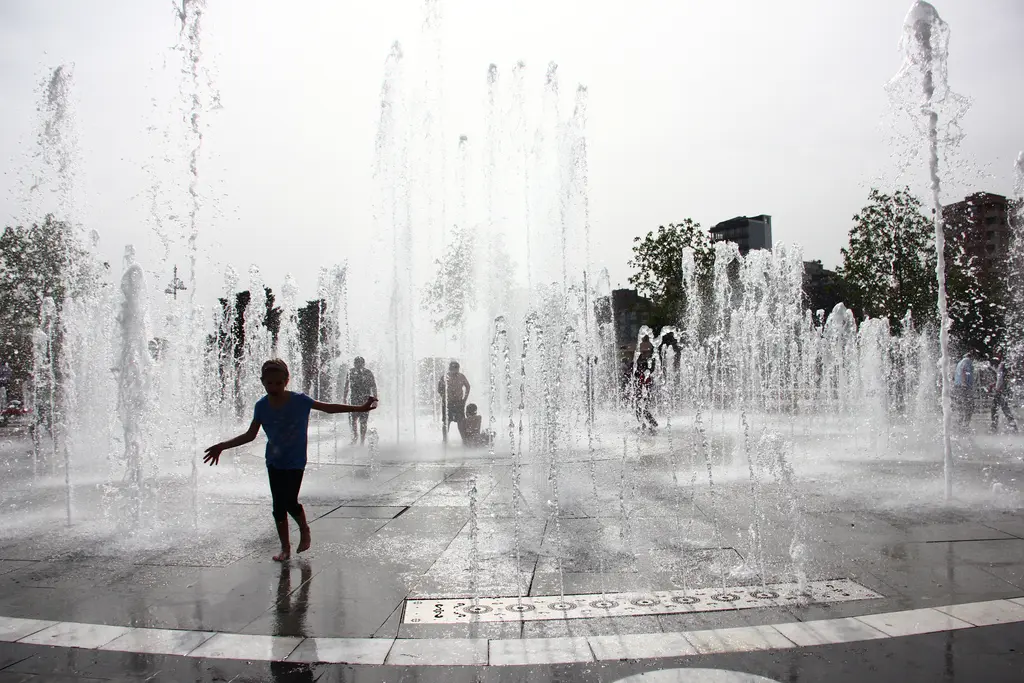 Göztepe Parkı'nda fıskiyeli havuz; yerden fışkıran su sütunları arasında koşan çocuklar ve arkada ağaçlar.