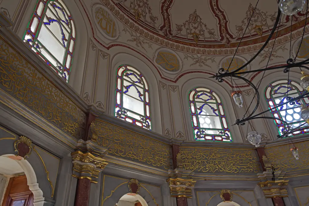 Mihrişah Valide Sultan Türbesi'nin içi; renkli camlı kemerli pencereler, yaldızlı yazı kuşakları, kalem işli kubbe ve asılı avize.