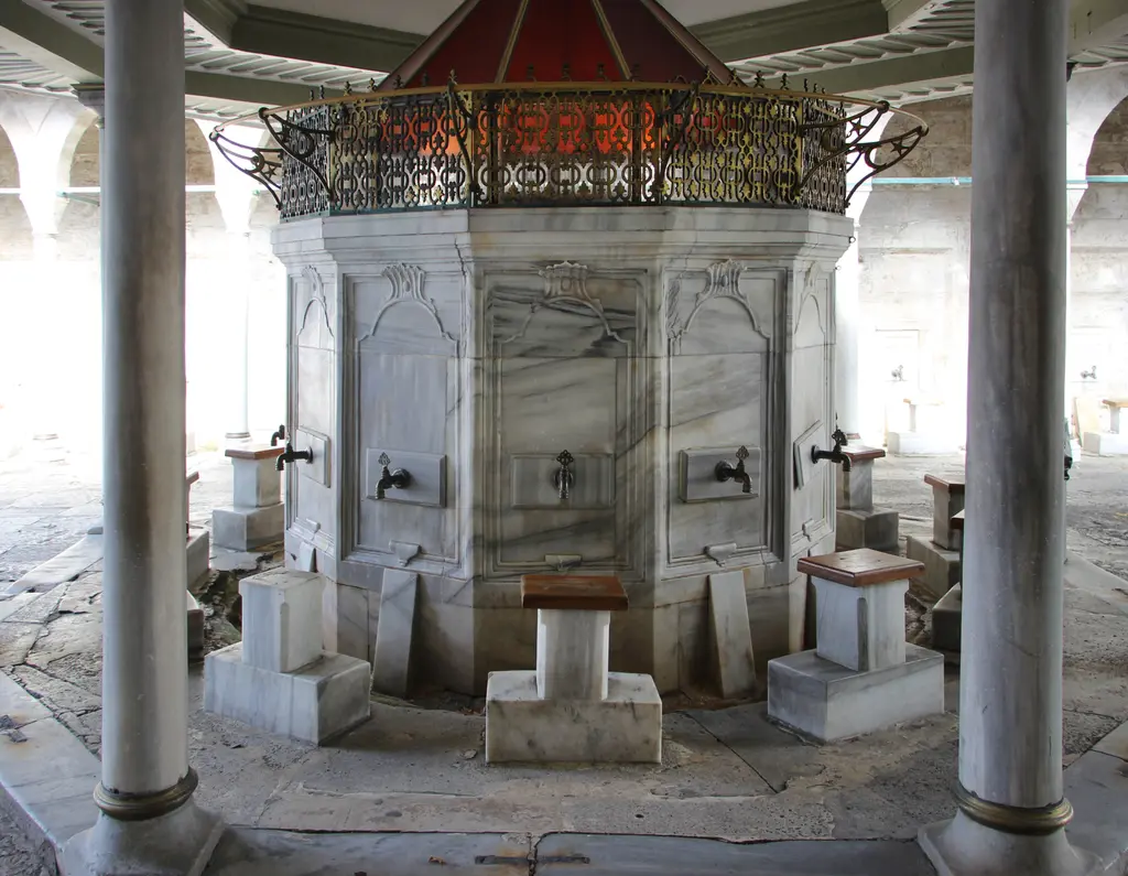 Kılıç Ali Paşa Camii'nin şadırvanı; mermer sütunlar arasında çok yüzlü haznesi, musluklar, taş oturma yerleri ve üstte demir şebeke.