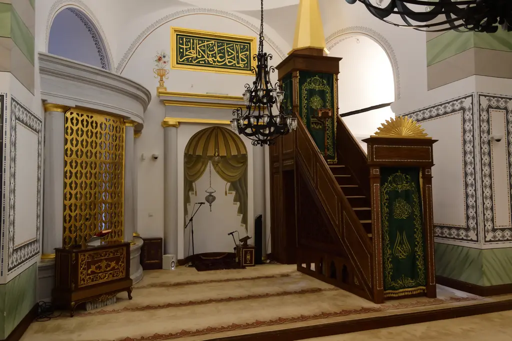 Koca Mustafa Paşa Camii'nin kıble duvarı; yaldızlı şebekeli, perde biçimli yeşil kavsaralı mihrap, sağında altın alemli konik külahlı ahşap minber, üstte siyah zeminli altın hat levhası.
