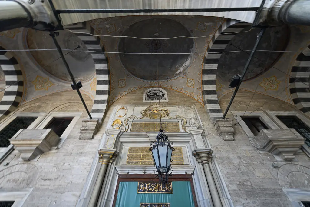 Eyüp Sultan Camii'nin son cemaat yeri; siyah-beyaz taş kemerler, kubbeler, asılı kandil ve taç kapı.