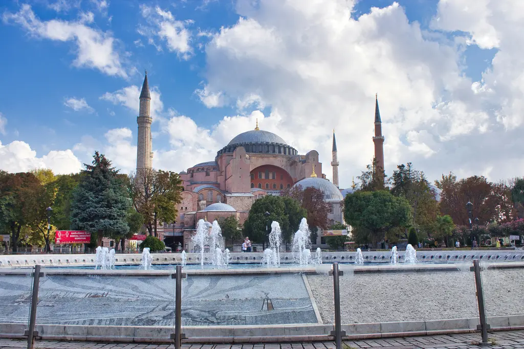 Sultanahmet'te meydandan Ayasofya; önde havuzdan yükselen su jetleri, çevrede ağaçlar ve arkada dört minareli taş yapı.