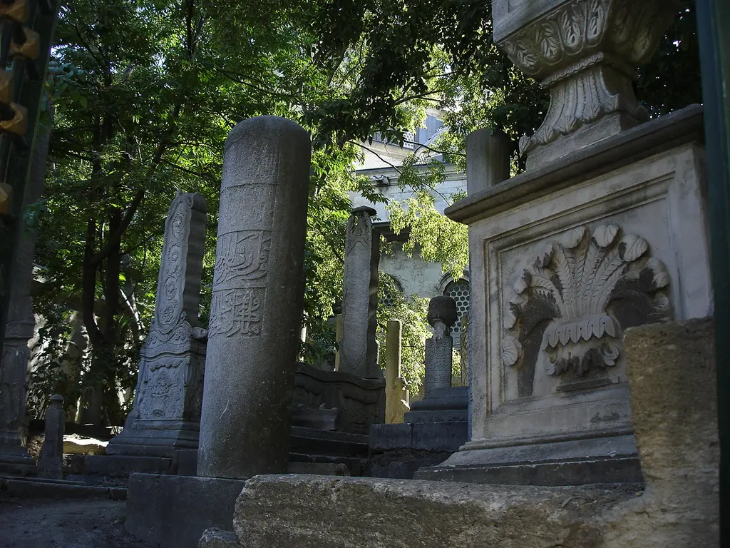 Eyüp Mezarlığı'nda kabirler; gölgede silindir biçimli mezar taşları, istiridye kabuğu kabartmalı lahit ve arkada ağaçlar.