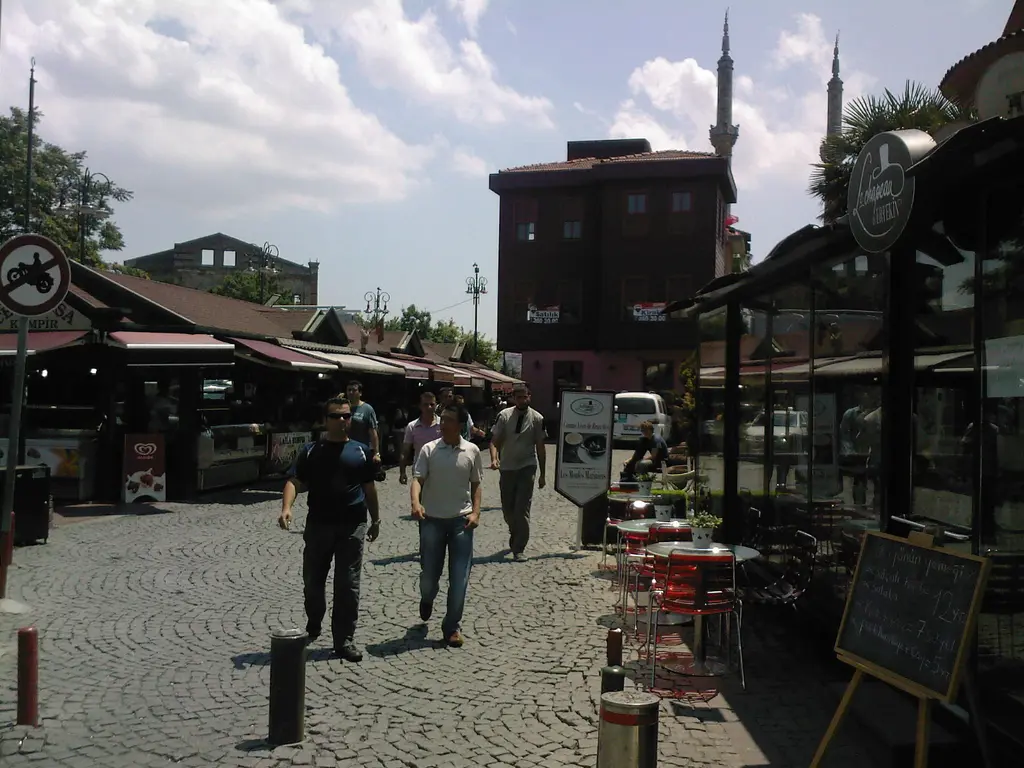 Ortaköy'de kumpirciler sokağı; tenteli tezgâhlar, taş döşeli yol, yürüyen insanlar ve arkada cami minaresi.