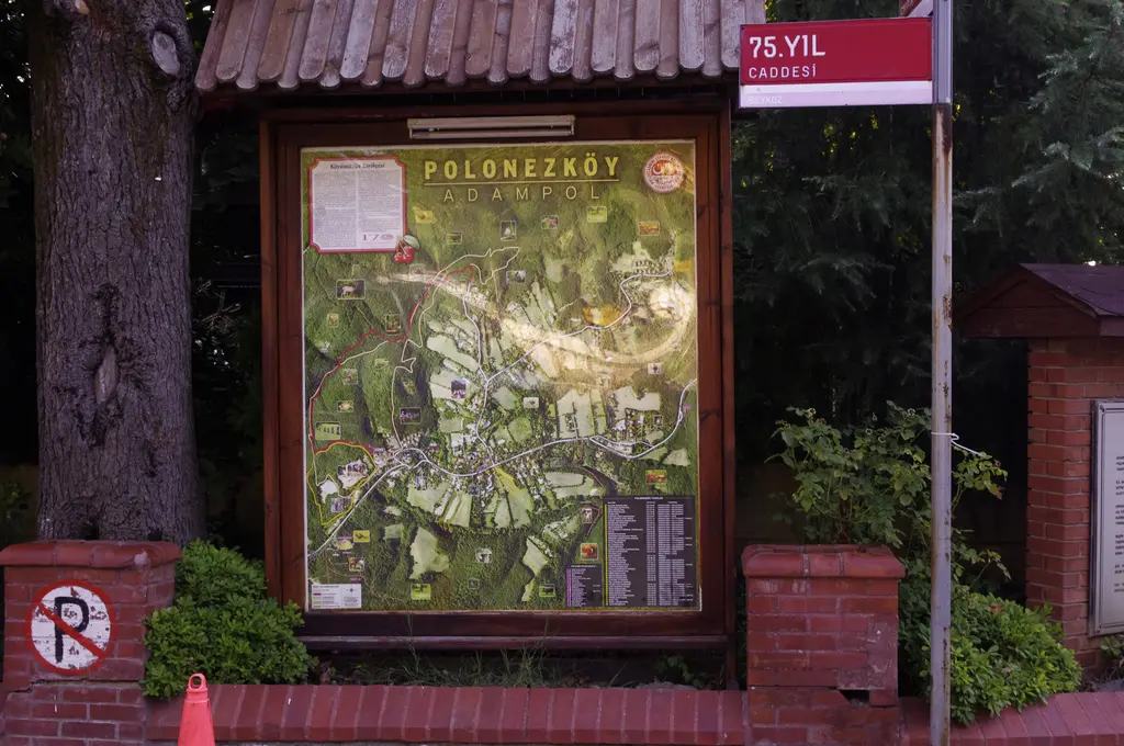 Polonezköy'de ahşap çatılı panoda "Polonezköy Adampol" başlıklı renkli köy haritası, yanında 75. Yıl Caddesi tabelası ve tuğla kaide.