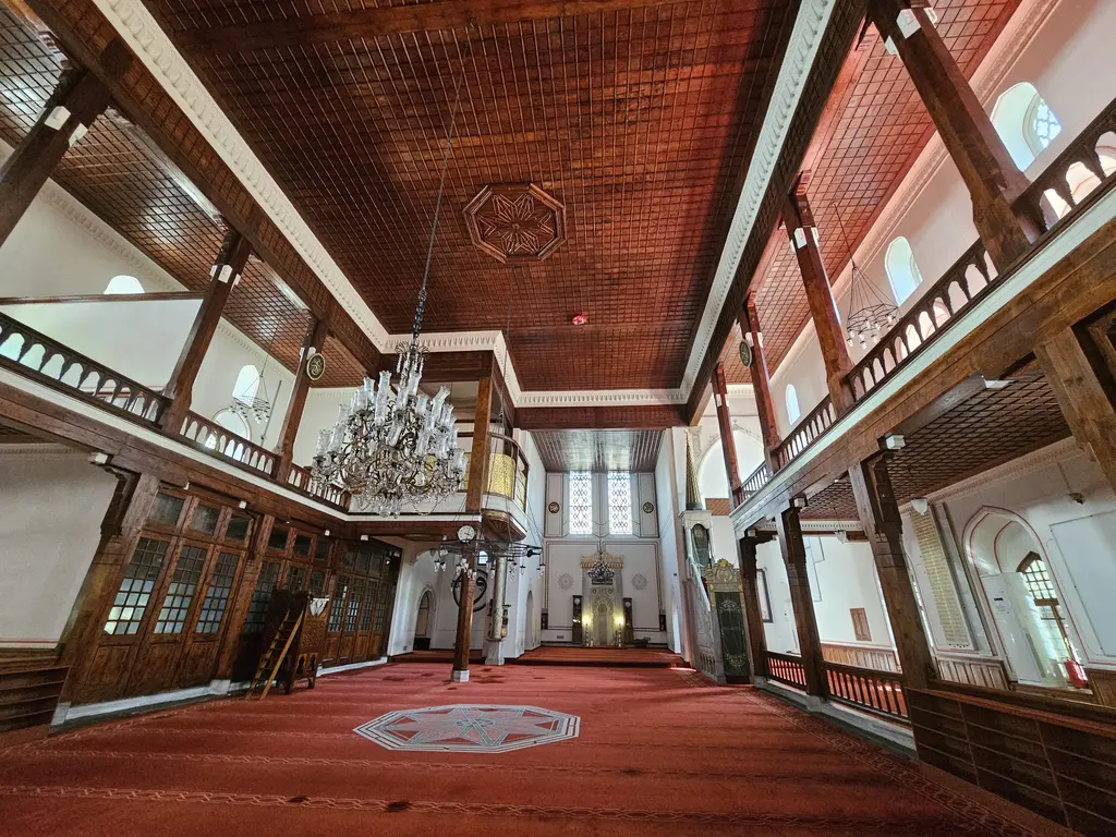 Arap Camii'nin harimi; uzun dikdörtgen mekân, kırmızı halı, iki yanda ahşap direkli mahfiller ve düz ahşap tavan.