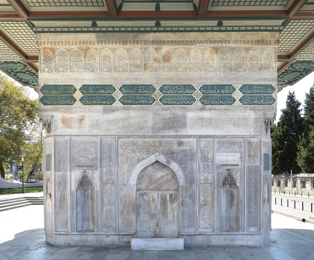Tophane Çeşmesi'nin bir cephesi; mermer gövdede orta niş ve yan nişler, üstte yeşil kartuşlu yazı kuşağı ve saçağın gölgesi.