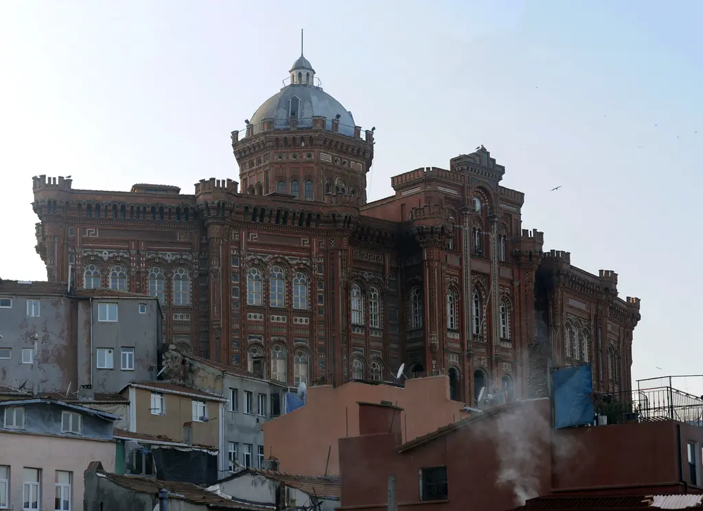 Okulun çatı hattı; kırmızı tuğla cephe, sıra sıra pencereler, köşe kuleleri ve ortada kurşun renkli kubbe.