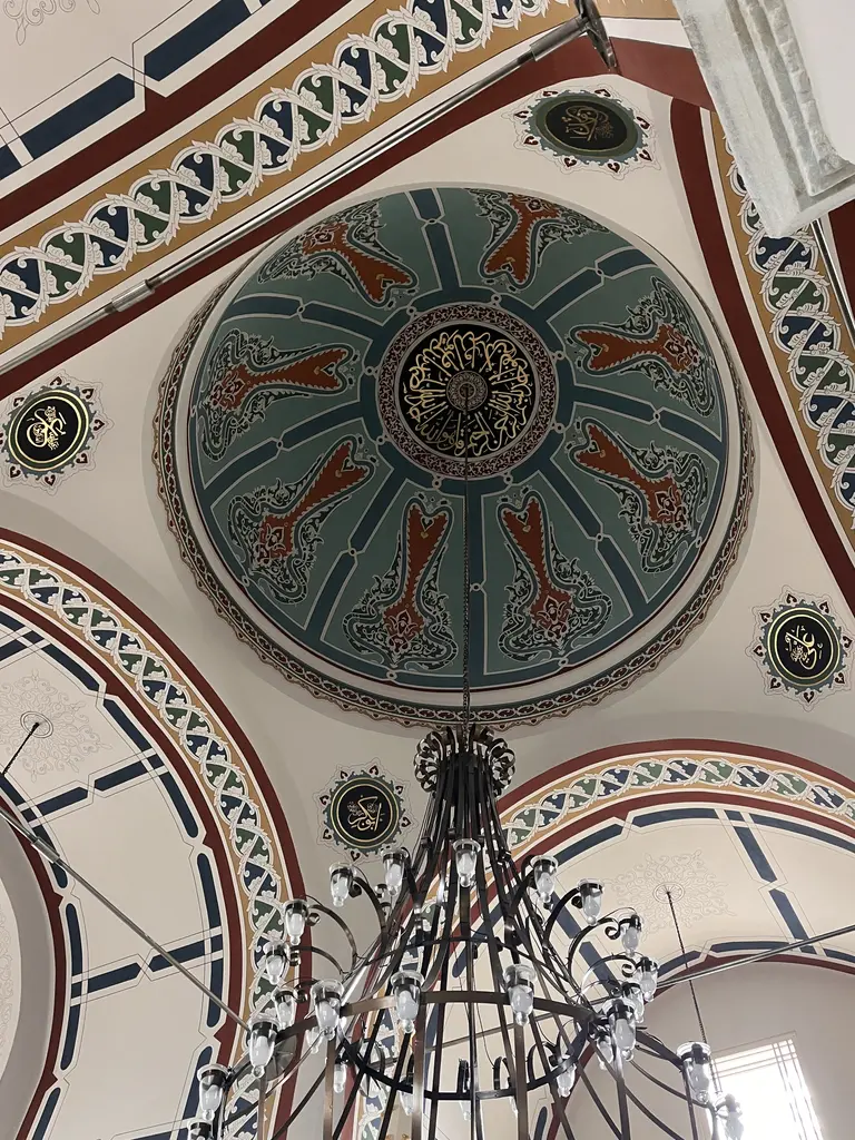 Atik Mustafa Paşa Camii'nin kubbesine alttan bakış; yeşil zeminli göbekte ışınsal kırmızı motifler, ortada altın hat madalyonu, çevrede kalem işli kemerler ve dövme demir avize.