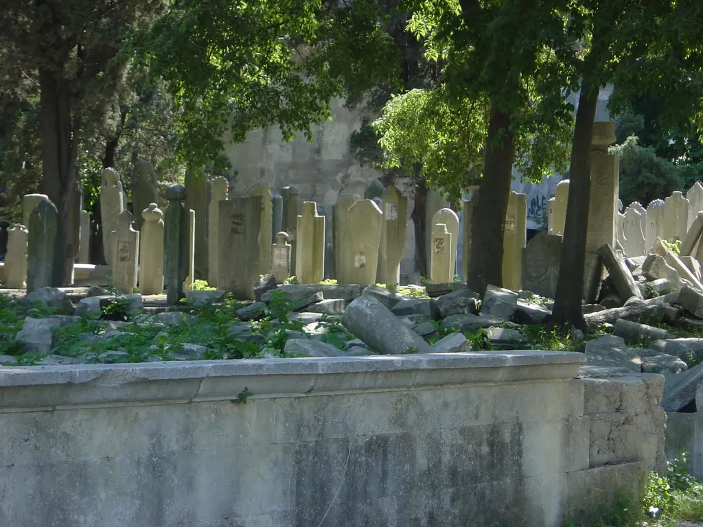 Eyüp Mezarlığı'nda tarihî mezar taşları; yan yana dikilmiş yazılı uzun taşlar, ağaç gölgesi ve önde alçak taş duvar.