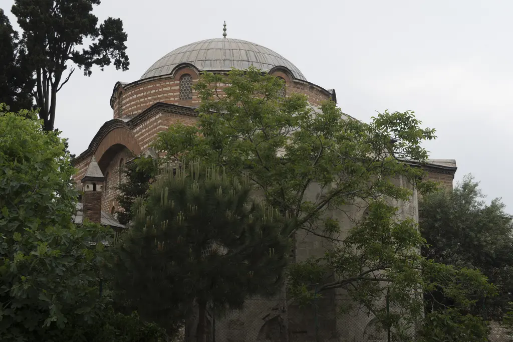 Rum Mehmed Paşa Camii; yoğun yeşil ağaçların ardından görünen kubbe, tuğla kasnak ve kemerli duvarlar.