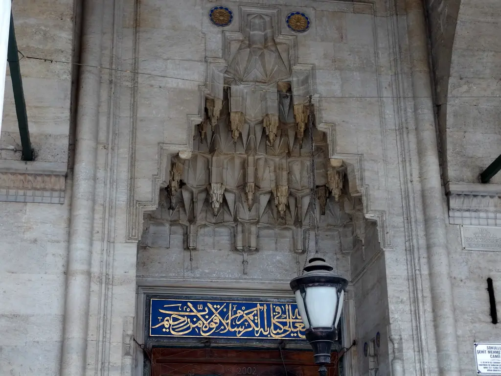 Sokullu Mehmed Paşa Camii'nde taçkapı; kademeli mukarnas dolgulu kavsara, altında çini hat kuşağı ve yanda demir fenerli duvar.