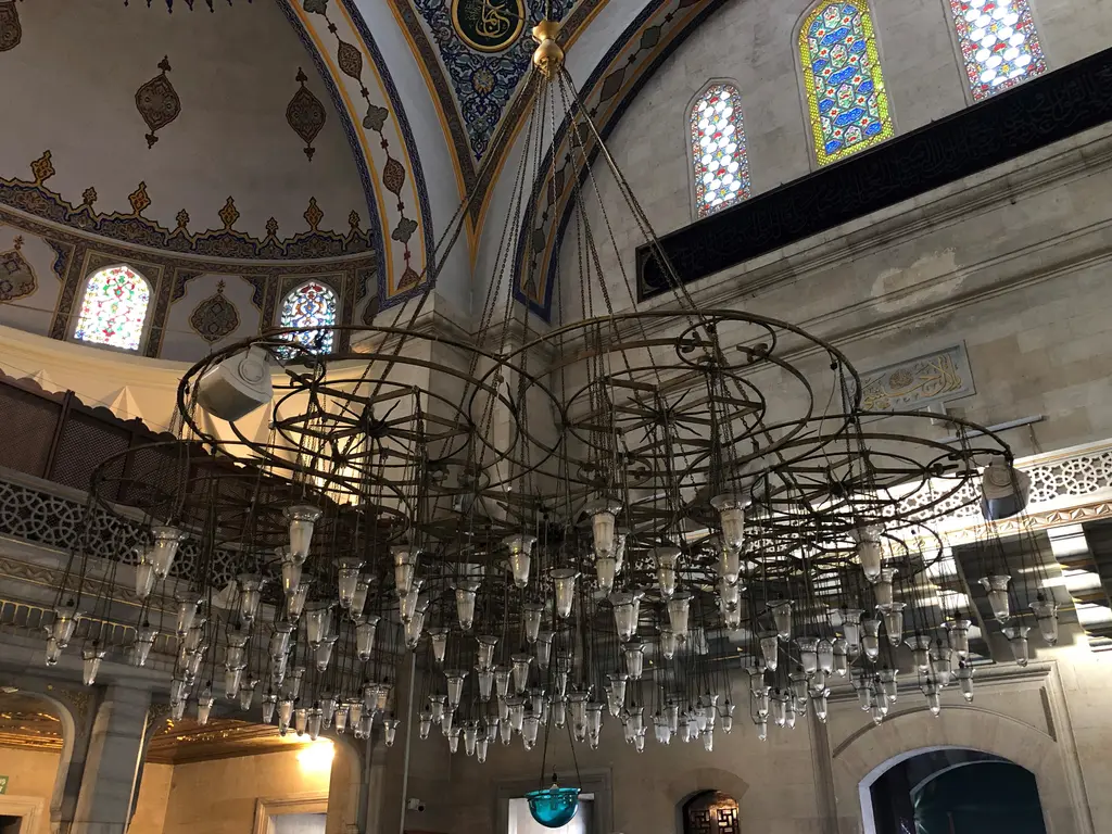 Şişli Camii'nin harimi; kubbeden sarkan büyük halka avize, vitraylı pencereler, kemerler ve kalem işi tavan.
