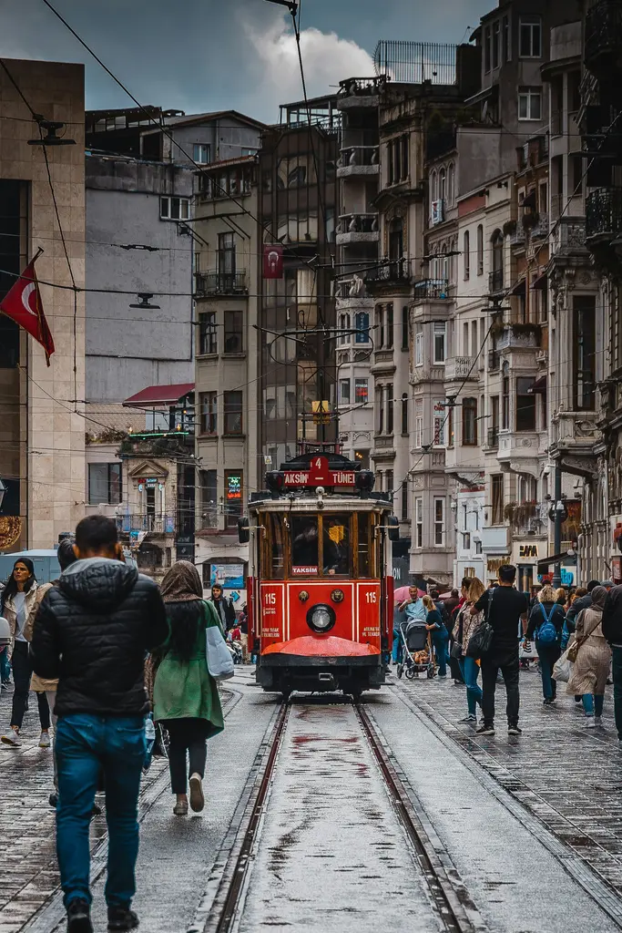 İstiklal Caddesi'nde kalabalığın ortasında ilerleyen nostaljik tramvay; iki yanda cumbalı cepheler, asılı bayraklar ve raylar boyunca yürüyen insanlar.