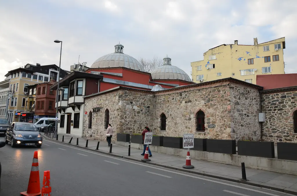 Ortaköy'de Hüsrev Kethüda Hamamı; kesme taş ve tuğla duvarlar, kurşun kaplı kubbeler, önde cadde ve trafik konileri.