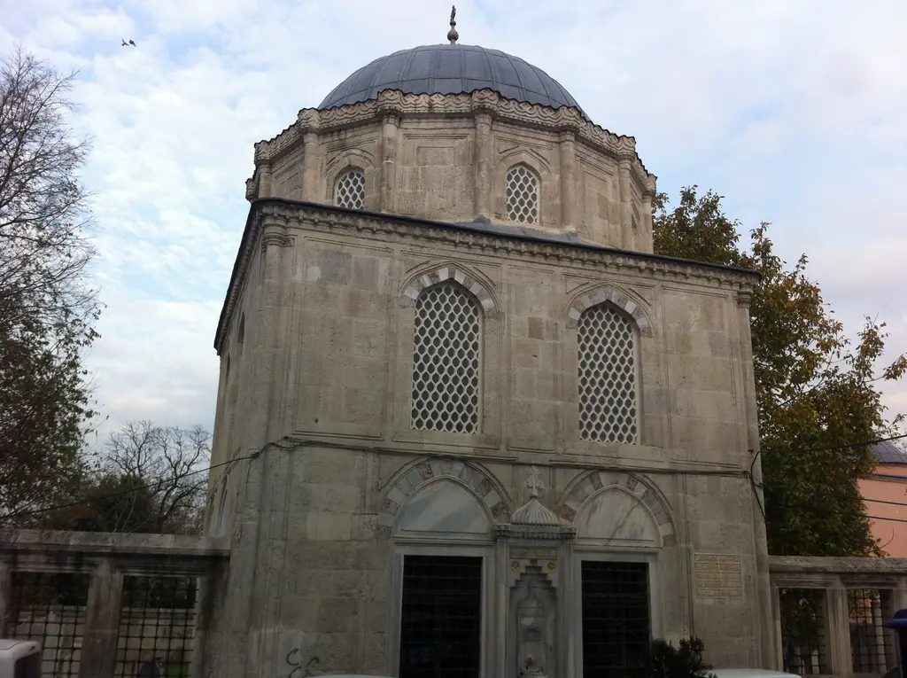 Eyüp'te Nakkaş Hasan Paşa Türbesi; kubbeli sekizgen kesme taş yapı, şebekeli pencereler, kemerli giriş ve ağaçlar.