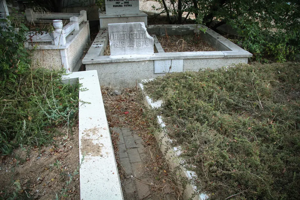Karacaahmet'te eski kabirler; mermer çerçeveli mezarlar, yazılı taşlar, kurumuş otlar ve yanlarda yeşillik.
