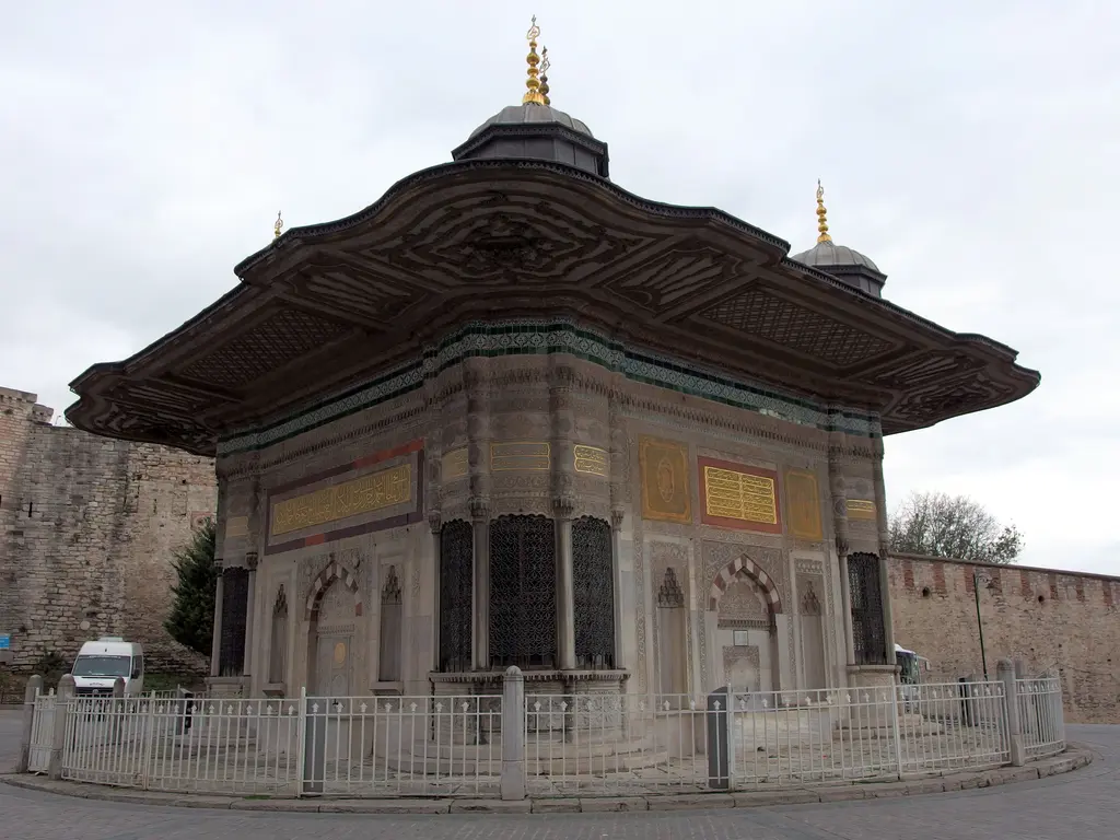 Çeşmenin köşeden görünüşü; iki cephe birden, yuvarlak taşan köşe sebili, saçağın altındaki işlemeli kuşak ve kurşun kaplı çatı.