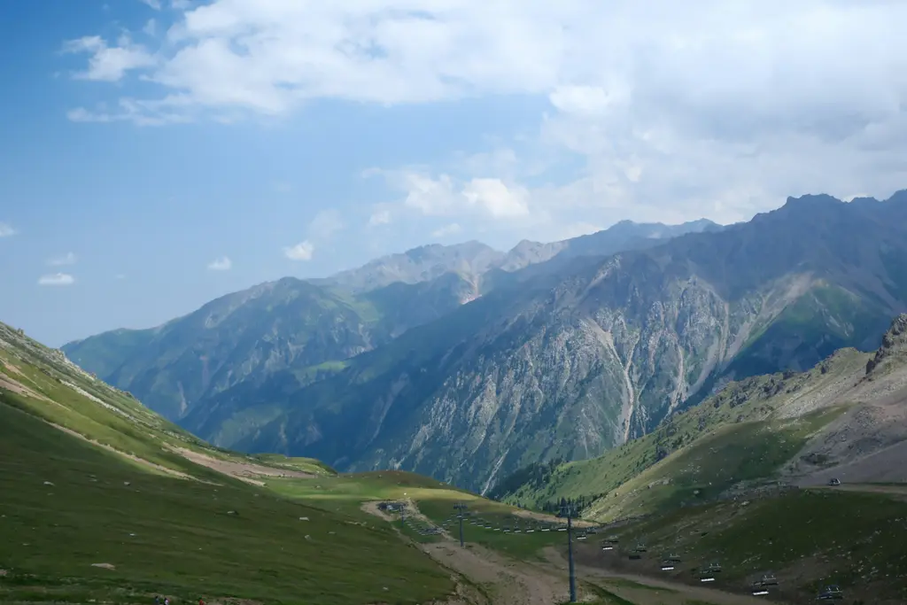 Tanrı Dağları'nda yeşil bir vadi; yamaçları kaplayan otlaklar, dipten geçen dar yol ve arkada üst üste sıralanan kayalık sırtlar.