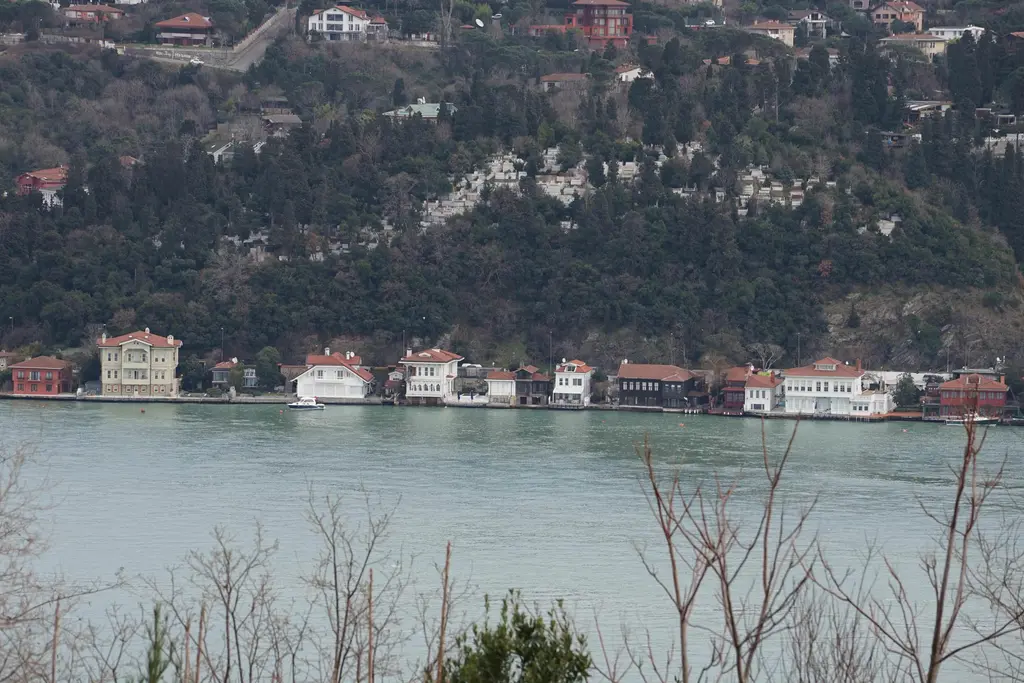 Karşı kıyıdan Kanlıca; koyu yeşil ağaçlarla kaplı yamaç ve kıyı boyunca dizilmiş beyaz yalılar.