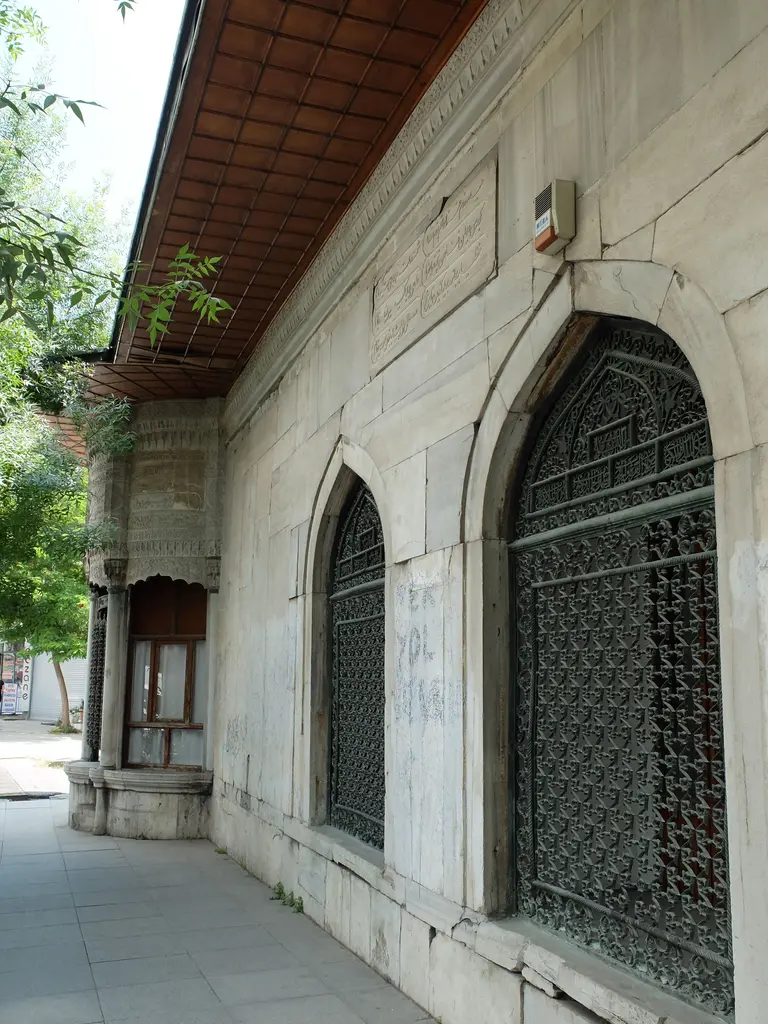 Türbenin cadde cephesi; mermer kaplı duvar, sivri kemerli pencereler, bitkisel desenli madeni şebekeler ve üstte kurşun kaplı ahşap saçak.