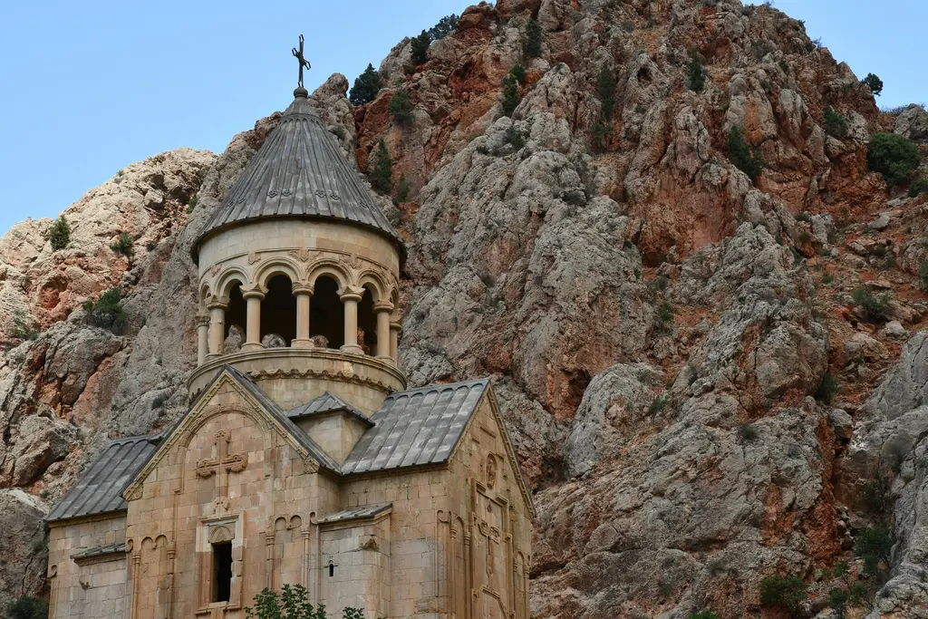 Noravank Manastırı'nın Surb Astvatsatsin kilisesi; açık renkli taştan gövde, üzerinde ince sütunlara oturan açık kemerli çan kulesi, hemen arkasında dik ve kızıl kayalık.