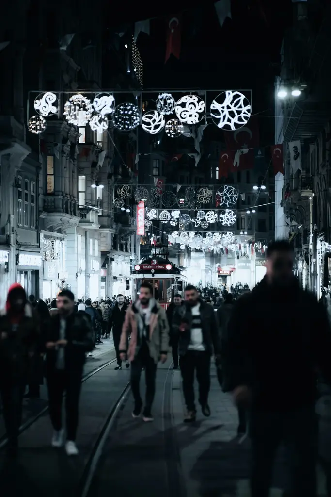 Gece İstiklal Caddesi; caddenin üstüne gerilmiş ışıklı süsler, iki yanda aydınlatılmış binalar ve yürüyen kalabalık.