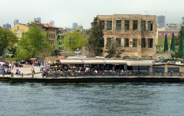 Boğaz'dan Esma Sultan Yalısı; boş pencereli yanık tuğla duvarlar, içinde cam yapı, önde rıhtım ve yanında ağaçlar.