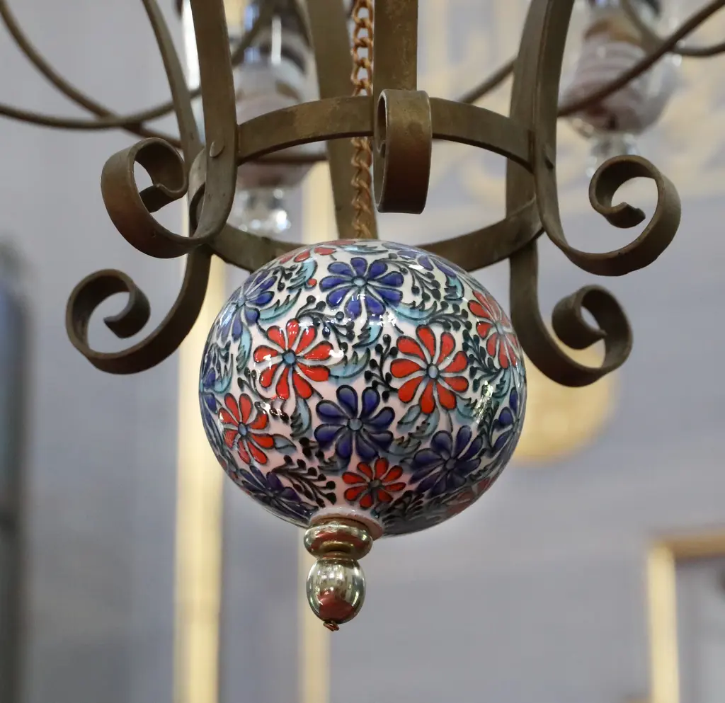 Atik Valide Camii'nde avize süsü; kıvrık demir kollar arasında kırmızı ve mavi çiçekli seramik top.