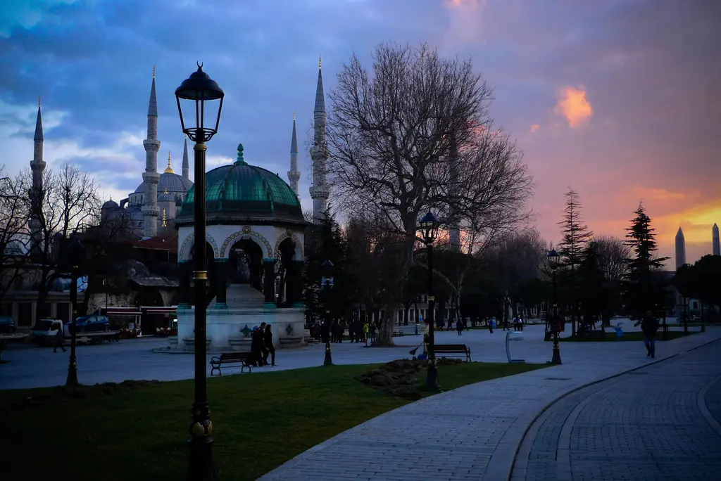 Gün batımında Sultanahmet Meydanı; ortada Alman Çeşmesi'nin kubbesi, arkada Sultanahmet Camii'nin minareleri, sokak lambası ve kızıl bulutlar.