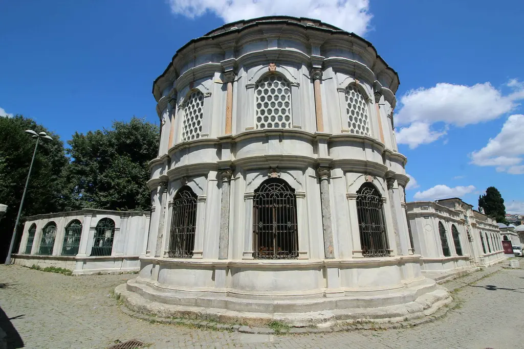 Mihrişah Valide Sultan Türbesi; geniş açıyla on iki yüzlü beyaz mermer gövde, kafesli üst pencereler, kubbe ve bulutlu mavi gökyüzü.