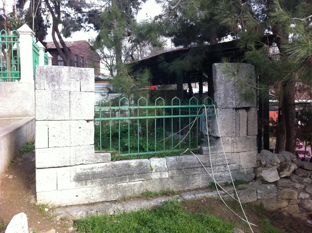 Eyüp'te Alaeddin Çelebi'nin açık türbesi; kesme taş duvarlarla çevrili kabir, yeşil demir parmaklık ve arkada ağaçlar.