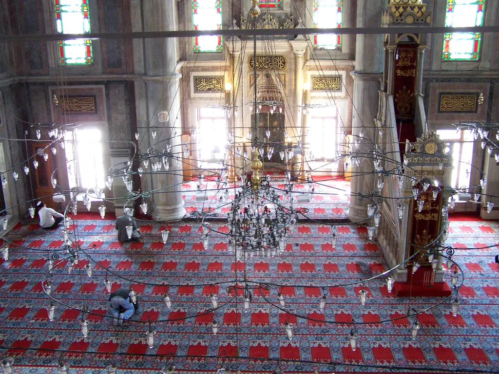 Laleli Camii'nin harimi; kırmızı halı kaplı geniş zemin, sıra sıra pencereler, sarkan avizeler ve ileride mihrap ile minber.