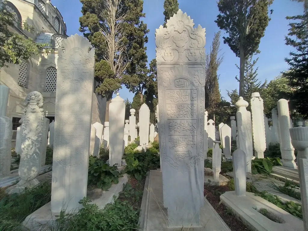 Atik Valide Camii'nin haziresi; servilerin arasında sıralanan sarıklı ve çiçekli mermer mezar taşları.