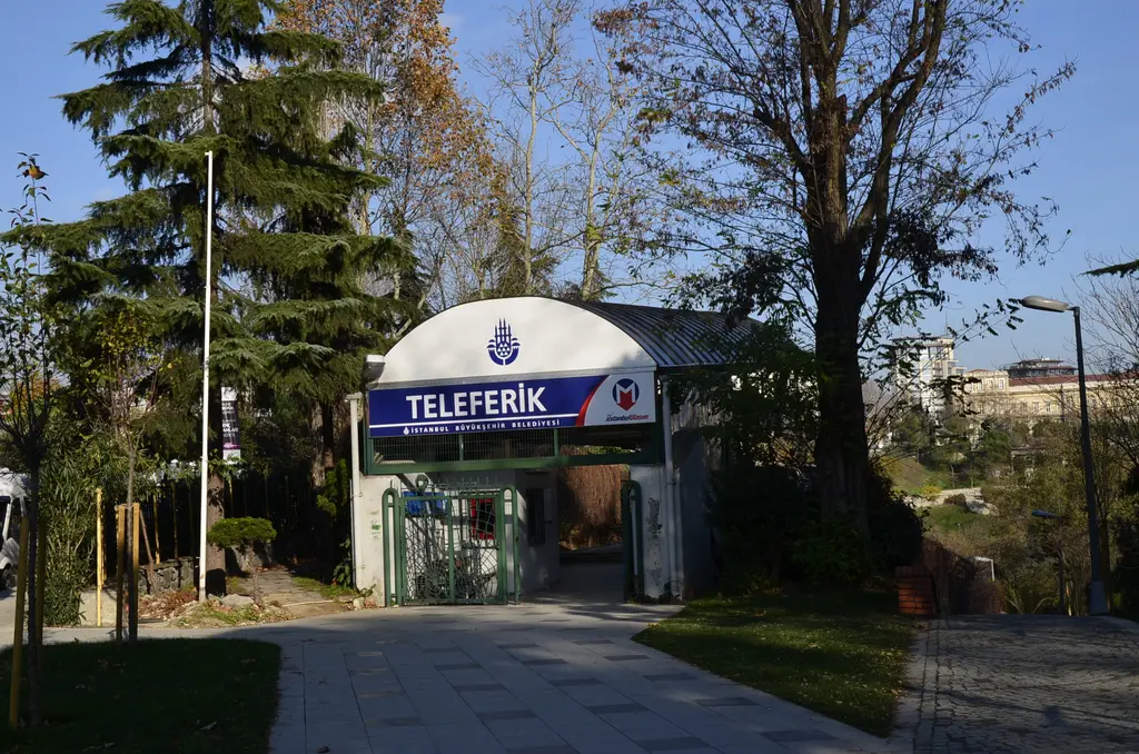 Maçka teleferiğinin Taşkışla istasyonu; ağaçlar arasında kemerli giriş, üstünde "Teleferik" tabelası ve belediye logosu.