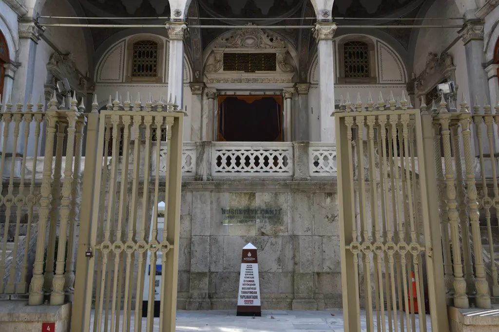 Nusretiye Camii'nin girişi; yaldızlı demir parmaklıklı kapı, arkada mermer sütunlu son cemaat yeri, balkonlu kemerli cephe ve taş merdiven.