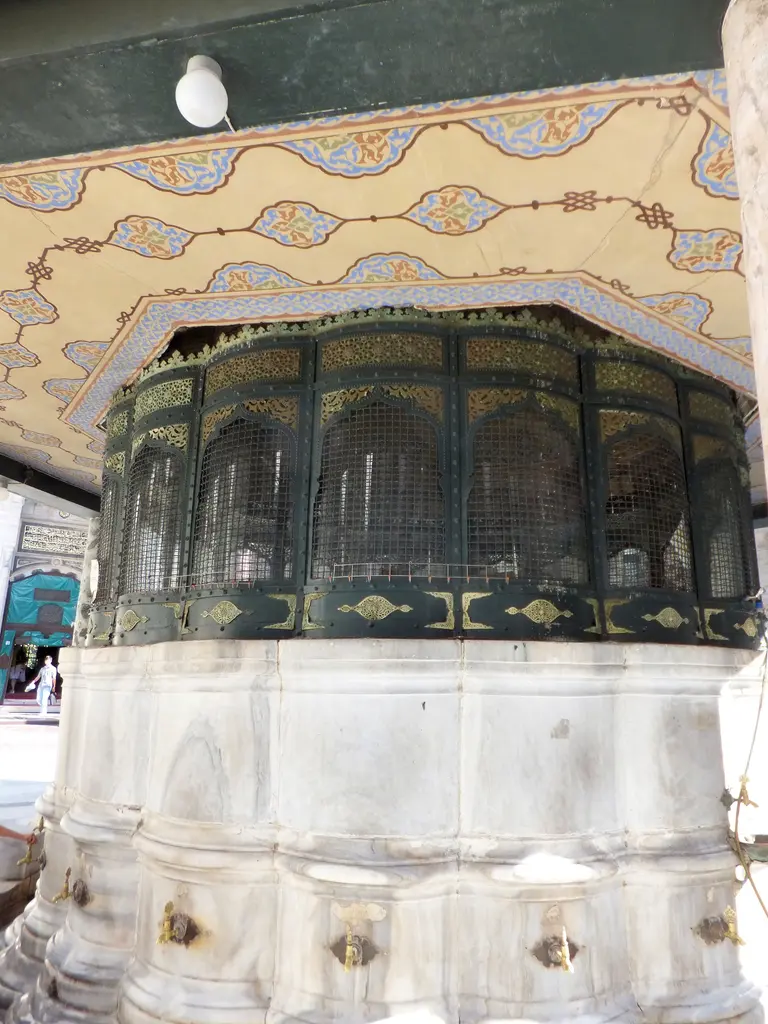 Şadırvan kubbesinin iç yüzü aşağıdan; boyalı bitkisel bezeme, yeşil boyalı ahşap kirişler ve dairesel madenî şebeke.