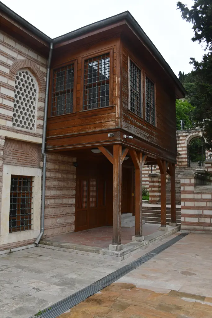 Şah Sultan Camii'nde ahşap çıkma; almaşık taş duvara bitişik iki katlı ahşap bölüm, direkler ve pencereler.