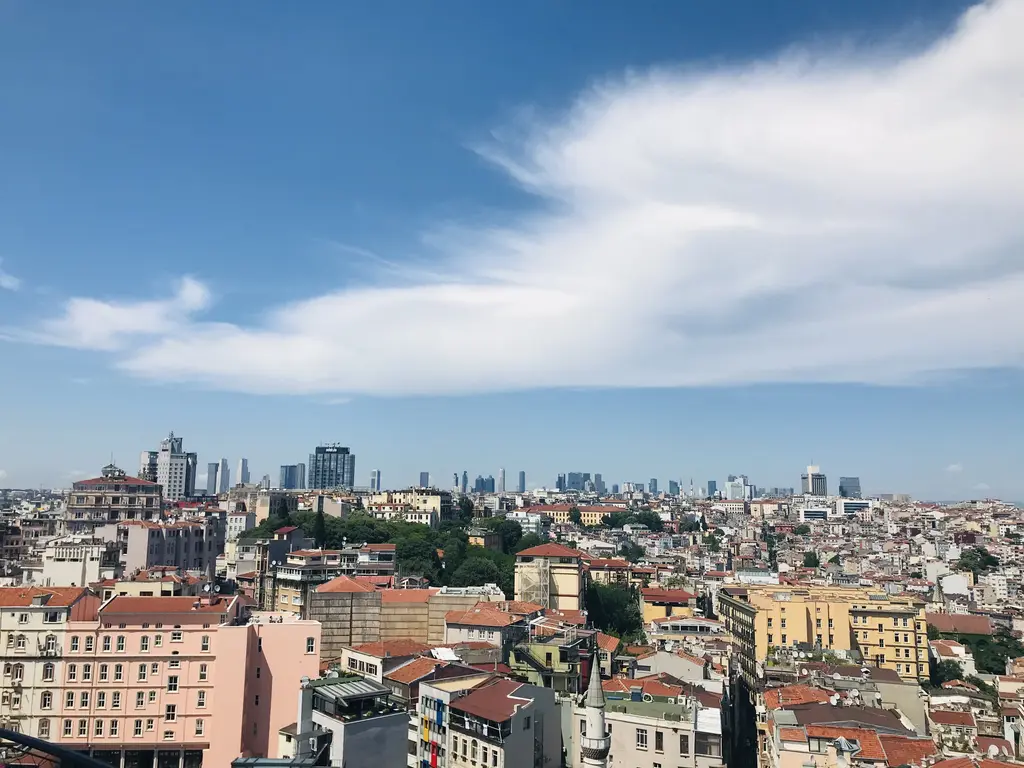 Galata Kulesi'nin terasından Beyoğlu; sık dizilmiş kiremit çatılı apartmanlar, ağaçlar ve ufukta yükselen gökdelenler.
