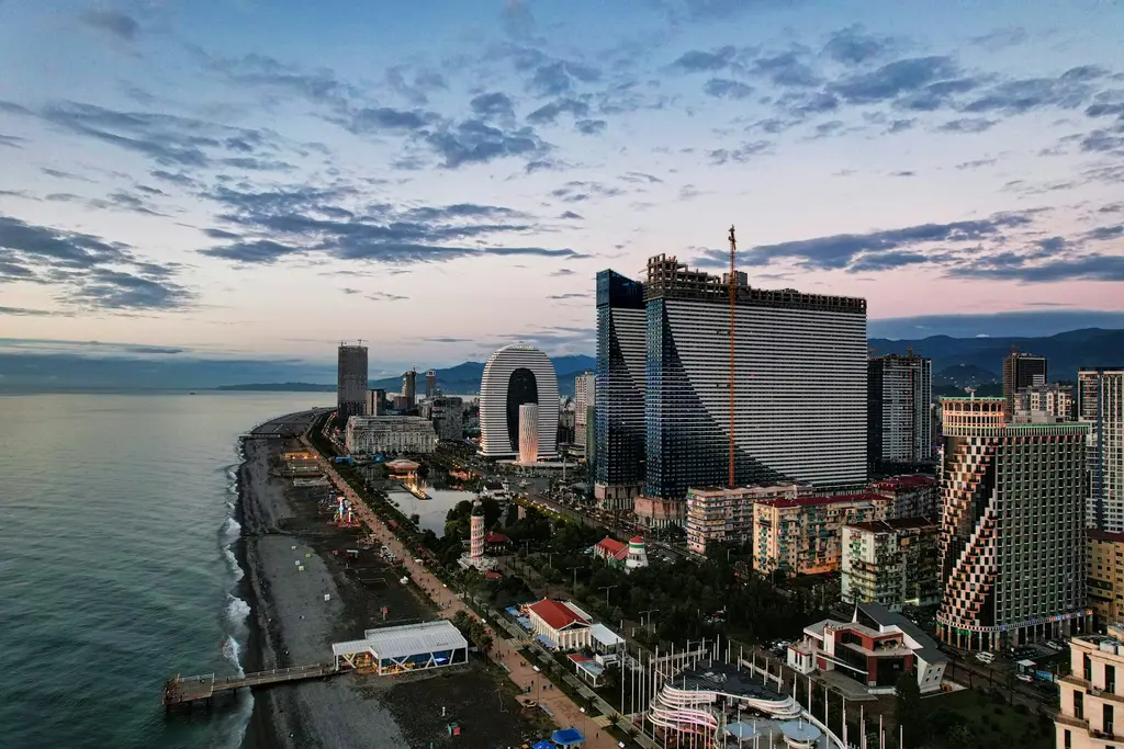 Batumi'de Karadeniz kıyısı; palmiyeli sahil, modern gökdelenler ve arkada Acaristan dağları.