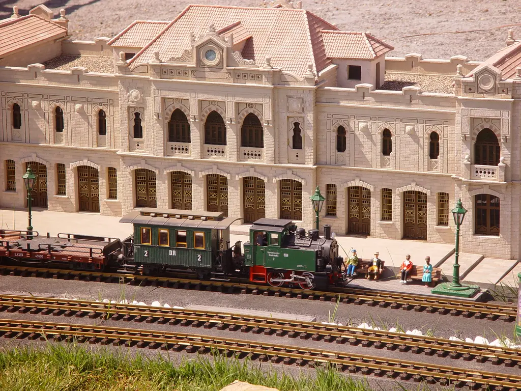 Miniatürk'te Şam Hicaz İstasyonu maketi; pembemsi bej taş cephe, yuvarlak saat, kiremit çatı, önde yeşil bir tren maketi ve raylar.