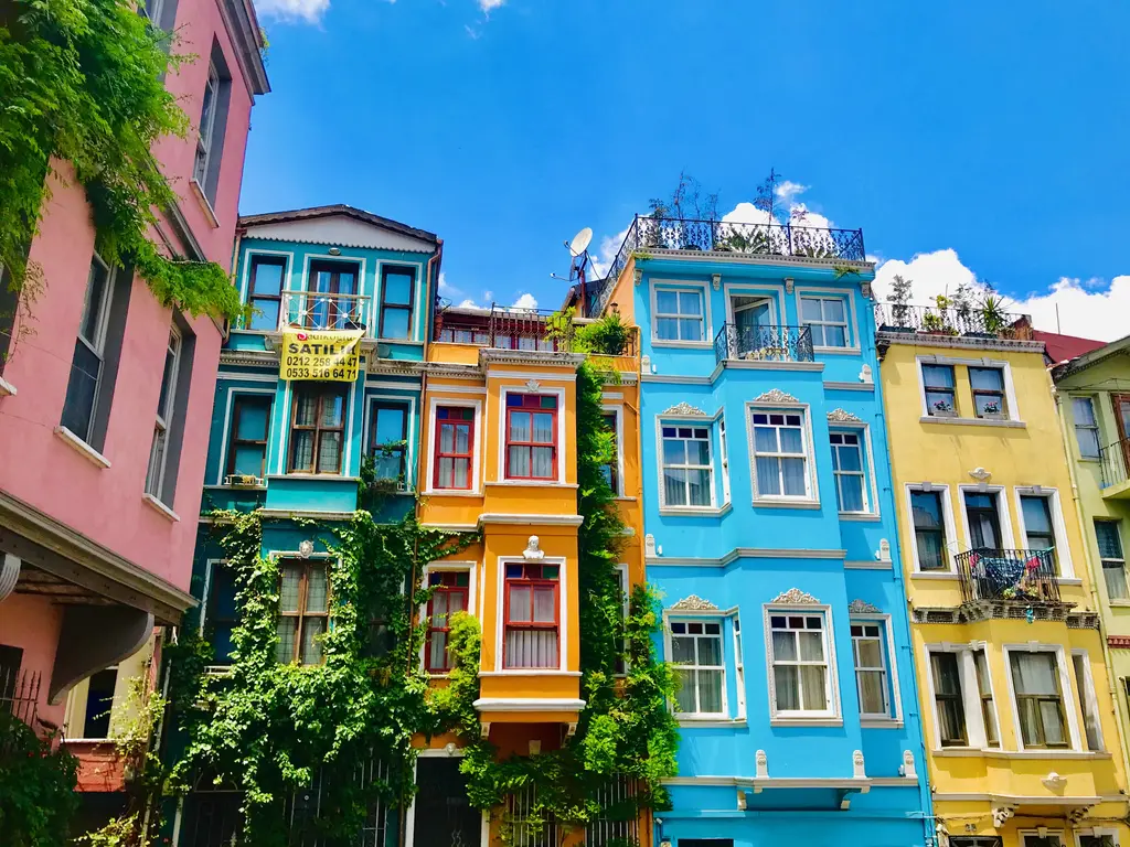 Balat'ta yan yana renkli evler; pembe, mavi, sarı ve turuncu cepheler, cumbalar, sarmaşıklı duvarlar ve mavi gökyüzü.