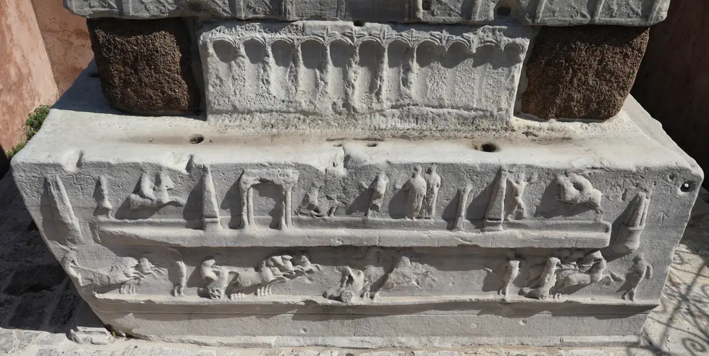 Dikilitaş'ın alt kaidesinde araba yarışı kabartması; atlı arabalar, dikili taşlar ve pistin iki ucundaki dönüş direkleri.