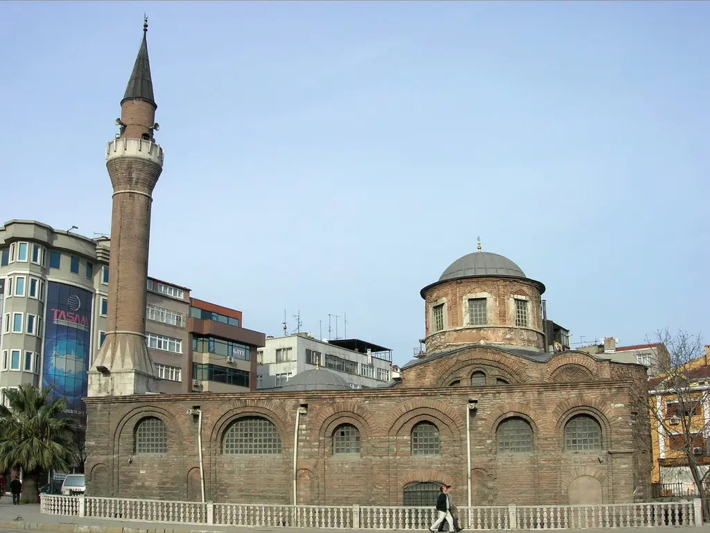 Fenari İsa Camii sokak seviyesinden; solda tuğla gövdeli minare, sağda kurşun kaplı kubbe, arada uzun kemerli pencere dizisi ve önde beyaz korkuluklu kaldırım.