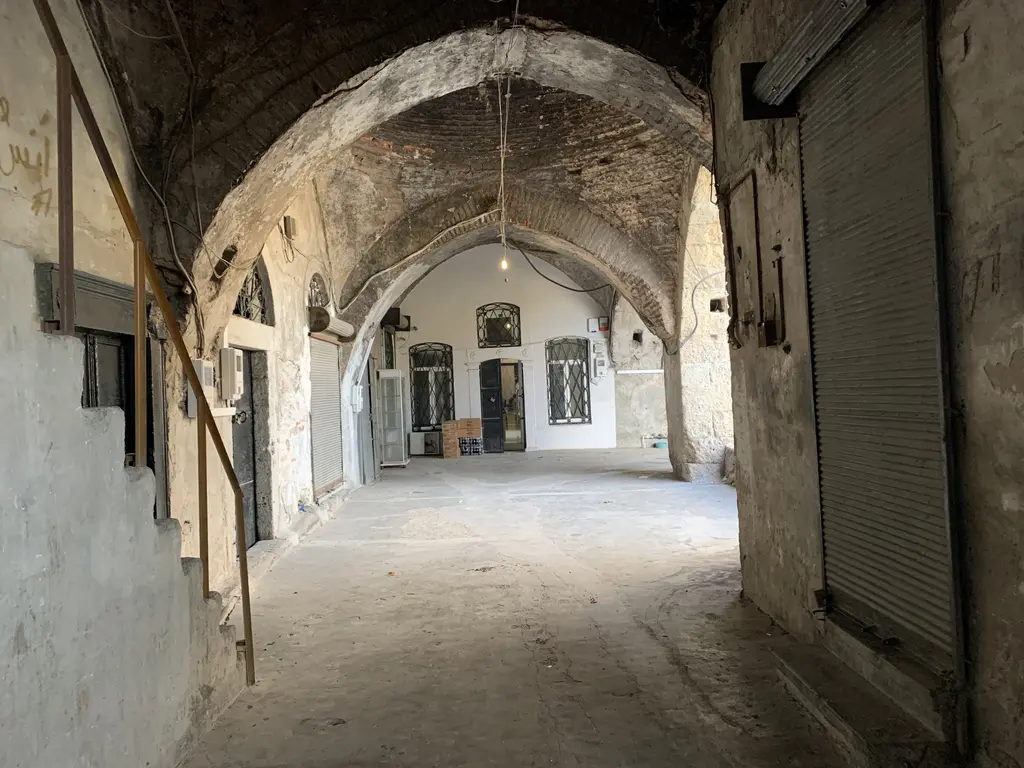 Büyük Valide Han'da bir kat koridoru; beyaza boyanmış tonoz, iki yanda kepenkli dükkân girişleri ve tavandan sarkan kablolarla lambalar.